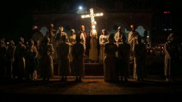 Várias pessoas religiosas em torno de uma cruz