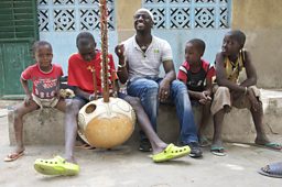 Griot Seckou Keita helping to teach his young cousins to play the Kora at his family home in Senegal