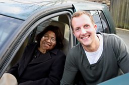 A man and an elderly woman posing by a car