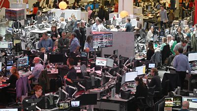 An overview scene of a busy 鶹 Broadcasting House newsroom, journalists working at desks, standing around the office taking meetings.