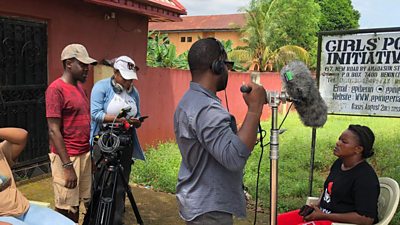 Production team in Nigeria recording a woman sitting under a sign that says 