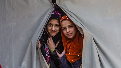 Girls peer out of a tent window in India