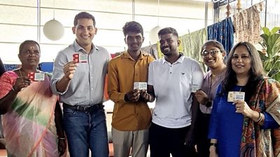 Three women in saris and three men show special business cards to the camera