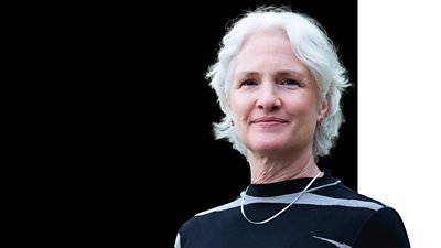 The ѿý's Chief Operating Officer looks straight ahead. She wears a necklace and a black and grey top