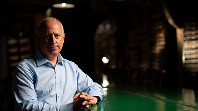 BBC Russia Editor, Steve Rosenberg, looks into the camera, behind a dark background in a blue collared shirt.