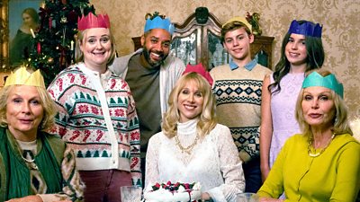 Seven people wearing paper crowns gathered around a dining table decorated for Christmas.
