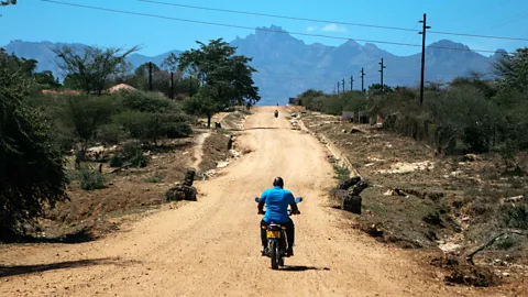 A man on a motorbike riding down a dirt track stretching towards mountains in the distance (Credit: Kang-Chun Cheng)