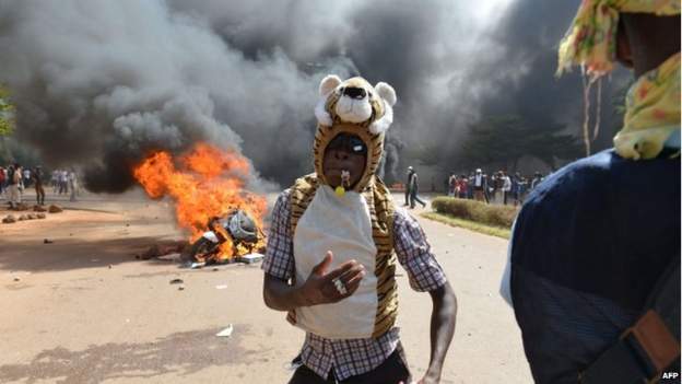A protester stands outside the parliament in Ouagadougou on 30 October 2014 as cars and documents burn outside.