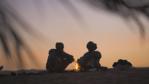 Silhouette of two nomadic people sitting around a camp fire at sunrise