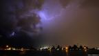 The night sky is lit by a huge fork of lightning above a city street in silhouette