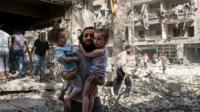 A Syrian man carries two girls as he walks across rubble in the northern city of Aleppo - 17 September 2015