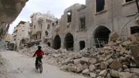 A boy rides a bicycle near damaged buildings in Aleppo, Syria. Photo: May 2016
