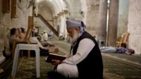 An elderly man reads the Quran in a West Bank mosque