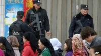 Uighur residents walk past Chinese SWAT policemen standing guard in a street of Yecheng in Xinjiang's Kashgar prefecture, in north west China, 29 Feb 2012