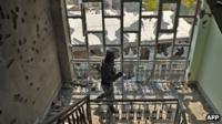 Man walks through buildings with shattered windows