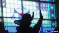 A figure in silhouette stands in front of a stained glass window