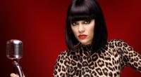 Jessie J in a publicity still for The Voice UK. She is wearing a leopard print top and holding a microphone.