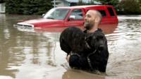 A man carries his dog in flood waters in Canada