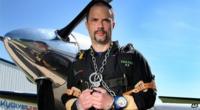 Anthony Martin stands in front of a plane with his hands chained together
