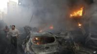 Lebanese citizens run past a burned cars and shops at the site of a car bomb explosion