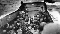 A landing barge, tightly packed with helmeted soldiers, approaches the shore at Normandy, France, on D-Day.