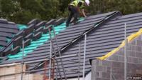 Construction site worker adds roof tiles to a housing development