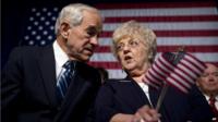 Former Texas Rep Ron Paul and his wife, Carol, talk in front of an American flag