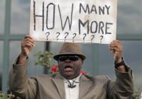 Man holding a sign that asks "How many more?"