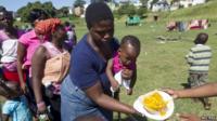 Women with children, who are the first to receive food, stand on a sports field in Chatsworth in the south of Durban