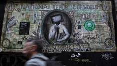 A man walks past a graffiti depicting a banknote in Athens,