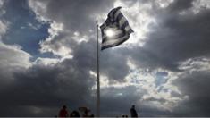 Tourists stand below a Greek flag floating in the wind at the Acropolis hill in Athens on 22 June 2015