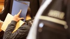 Defendant holds a file folder in front his face in the court room in Cologne