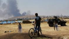 A boy on a bike watches smoke over the Syrian town of Kobane from Turkish territory, 27 June