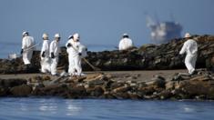 Workers on a beach with an oil platform in the background