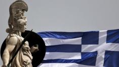 A Greek national flag flutters next to a statue of ancient Greek goddess Athena, in Athens