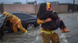 Un bombero evacúa a una mujer de su automóvil, que quedó atrapado en una inundación.