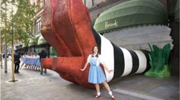 Mujer vestida como Dorothy posa frente a un modelo gigante de los zapatos rojos al lado de la tienda Harrods.