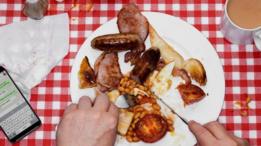 Una persona comiendo un tradicional desayuno inglés, con huevos, salchichas, frijoles y tocineta