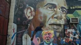 صورة أوباما على حائطة ويمر رجل يحمل صورة مرسومة لترامب