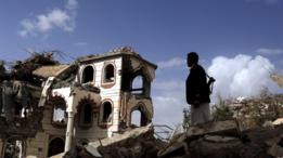 مسلح يمني يقف أمام مبنى دمر في قصف لطائرات التحالف الذي تقوده السعودية