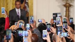 Decenas de celulares toman fotografías de Obama quien aparece en el fondo de manera borrosa.