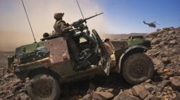 مركبة عليها جندي ومدفع رشاش وطائرة هليكوبتر في منطقة جبلية