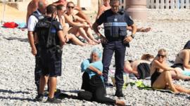 Los policías en Niza conversan con la mujer vestida en la playa.
