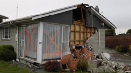 The chimney has fallen of a damaged house that has a red 'Danger' mark written on its side