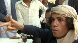 A Yemeni man, amongst a group of men - discussing how US bombing has affected their lives