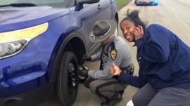 Picture of a white police officer changing a car tyre for an African American woman