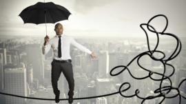 Business man with umbrella balancing on tightrope