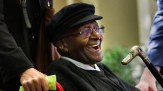 Desmond Tutu smiles in a wheelchair