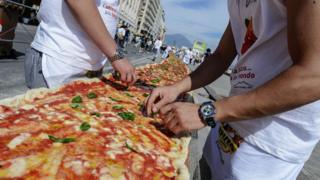 Men adding toppings to the pizza.