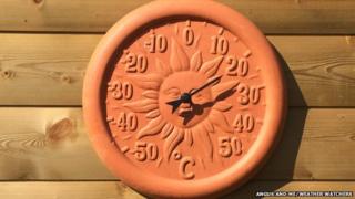 A terracotta garden thermometer with the sun's face, which reads 20C